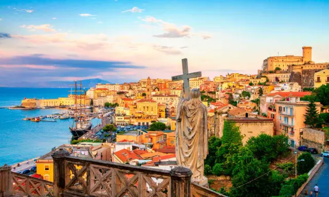 Statua con croce domina la vista di Gaeta, perfetta per una gita fuori porta da Roma. Porto, case colorate e castello sullo sfondo.