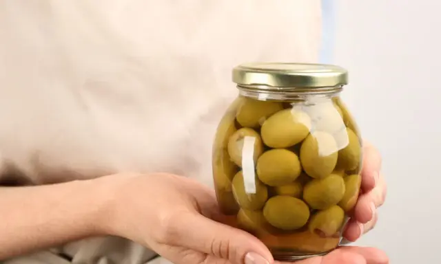 Mani che tengono un barattolo di olive verdi in salamoia per olive, pronte per essere gustate.