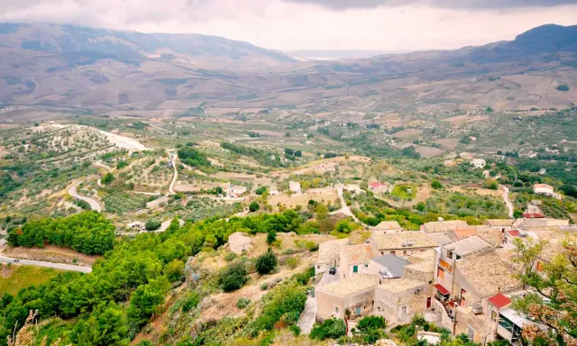 Panoramica di Contessa Entellina, un borgo siciliano tra colline verdi e campi coltivati, con case dai tetti in cotto e una strada tortuosa.