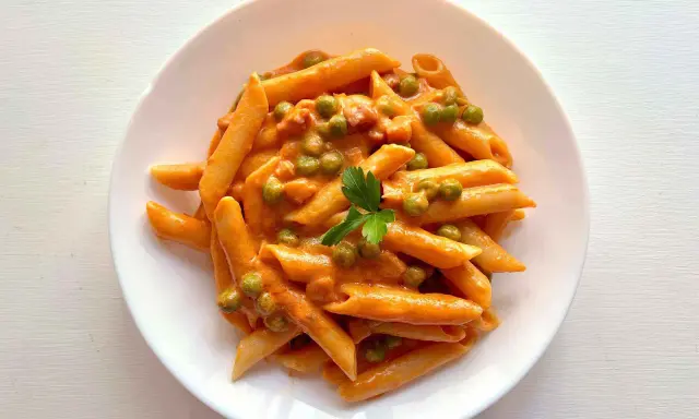Penne ai 7 peccati: un piatto di pasta cremosa con piselli e un tocco di pomodoro, guarnito con prezzemolo fresco.