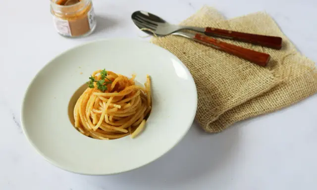 Spaghetti alla bottarga, un piatto semplice ma gustoso, pronto per essere assaporato. Un vasetto di bottarga in polvere e posate completano la scena.
