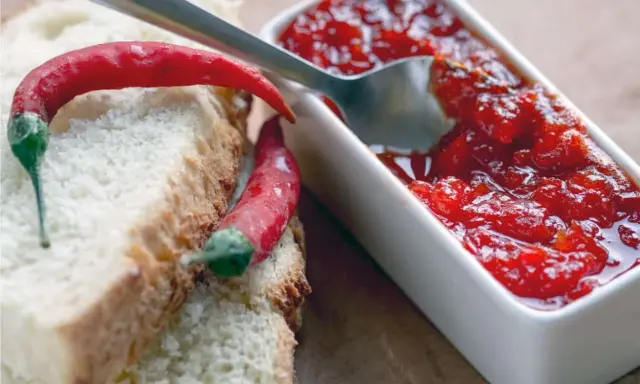 Fette di pane con peperoncini rossi e una ciotolina di marmellata di peperoncino, pronta per essere gustata.