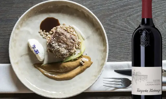 Piatto gourmet con carne, cereali e salsa, accanto a una bottiglia di Lagrein Riserva. Perfetti lagrein abbinamenti per un'esperienza culinaria raffinata.
