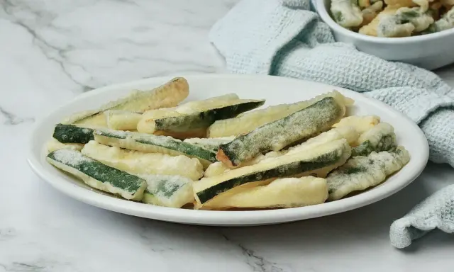 Zucchine fritte in pastella dorata, croccanti e invitanti, servite su un piatto bianco.