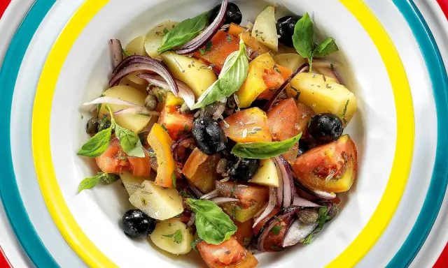 Insalata eoliana con patate, pomodori, olive nere, cipolla rossa e basilico fresco, servita in un piatto colorato.