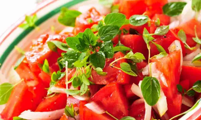 Un'insalata di pomodori freschi e succosi, condita con cipolla bianca e profumata erba aromatica.