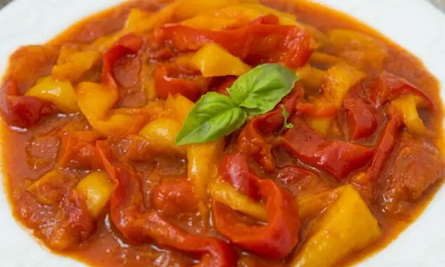 Peperonata ricetta della nonna: peperoni rossi e gialli cotti lentamente in un sugo saporito, guarniti con basilico fresco.