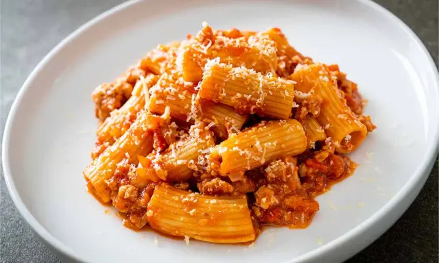 Un piatto di pasta alla zozzona, con rigatoni conditi con un ricco sugo di carne e pomodoro, spolverati di parmigiano.