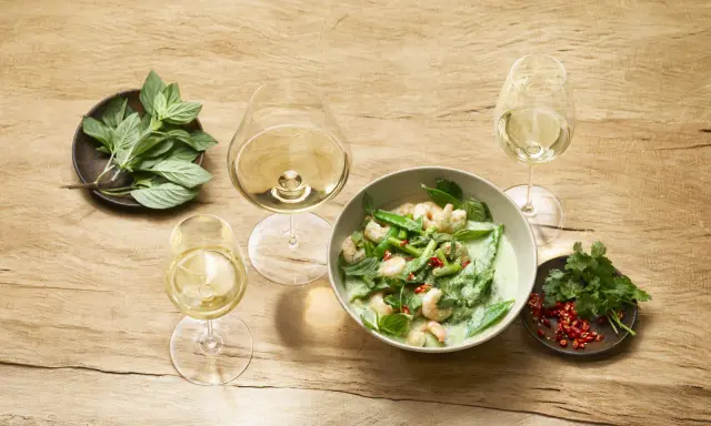 Un curry verde con gamberi e verdure, accompagnato da bicchieri di vino bianco, evoca le fresche **sauvignon blanc caratteristiche**.