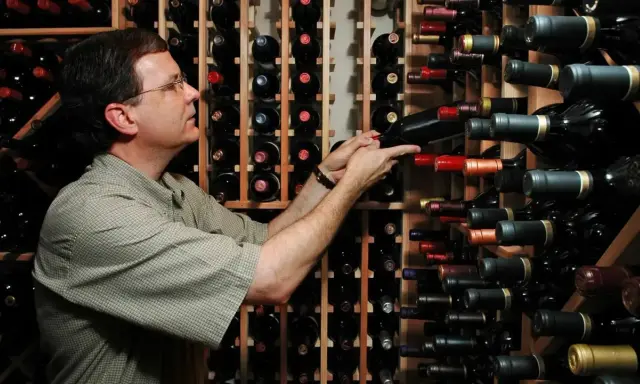 Uomo in cantina sceglie una bottiglia, pensando se il suo chardonnay è fermo o frizzante.