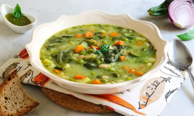 Un fumante minestrone genovese, ricco di verdure fresche, piselli, carote e fagioli, servito con pesto e pane tostato.