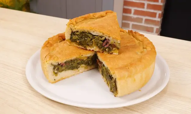 Una fetta di pizza di scarola, ricca di verdure e olive, su un piatto bianco.