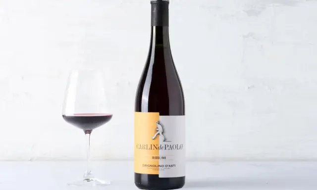 Calice di vino rosso accanto a una bottiglia di Grignolino d'Asti Carlin de Paolo. Un vino che ricorda il barbera vitigno per la sua vivacità.