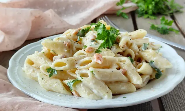 Piatto di pasta panna e salmone, guarnito con prezzemolo fresco, servito su un piatto bianco.