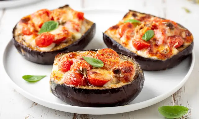 Melanzane ripiene vegetariane, gustose e colorate, con pomodorini e formaggio filante, guarnite con basilico fresco.