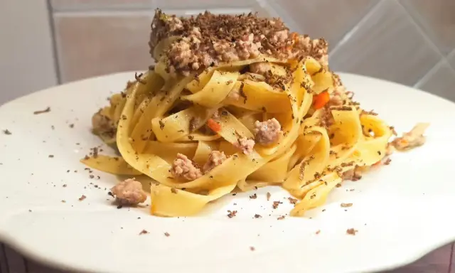 Tagliatelle al ragù con scaglie di tartufo nero, un piatto ricco e profumato, pronto per essere gustato.