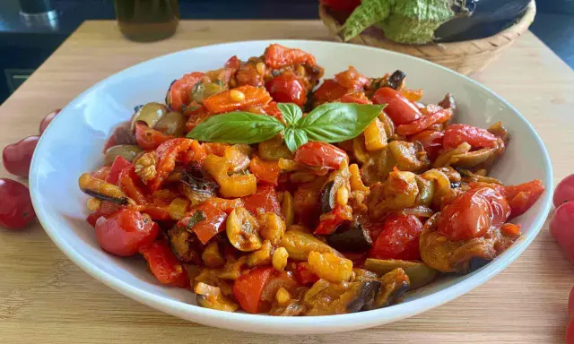 Caponata siciliana ricetta della nonna: un piatto colorato con melanzane, peperoni, pomodorini e basilico, pronto per essere gustato.
