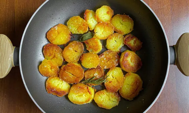 Patate dorate e croccanti in padella, pronte per deliziose ricette con patate. Un rametto di rosmarino aggiunge profumo.