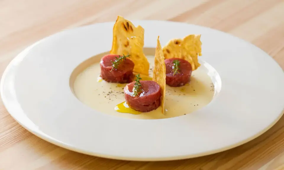 Tre cilindri di tartare di manzo, guarniti con timo, su una crema chiara e croccanti cialde. Un'idea su come condirla.