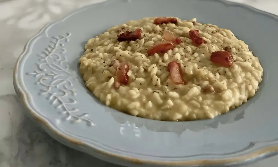 Un cremoso risotto con ceci e pancetta croccante, servito su un piatto azzurro decorato.