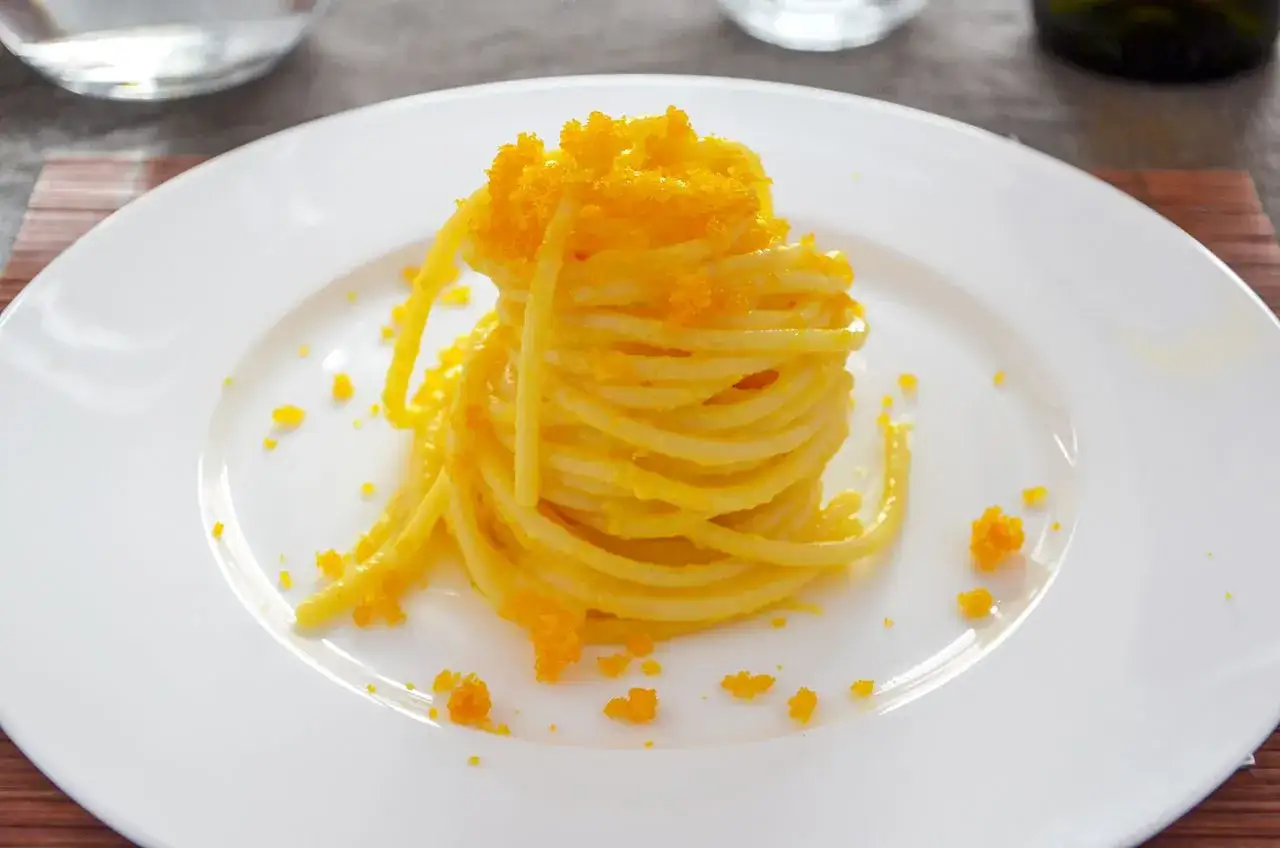 Un nido di spaghetti alla bottarga, guarnito con uova di muggine sbriciolate, su un piatto bianco.