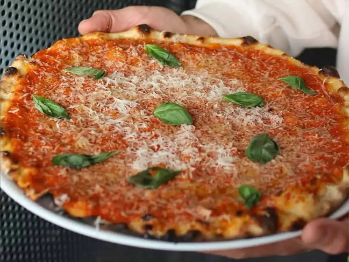 Pizza romana con pomodoro, parmigiano e basilico fresco. Semplici ingredienti per un sapore autentico.