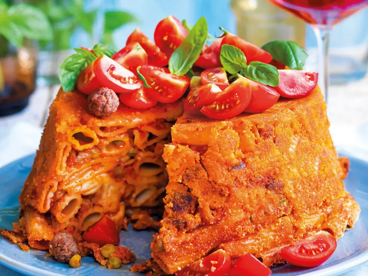 Un invitante timballo di pasta, ricco di sugo e decorato con pomodorini freschi e basilico.