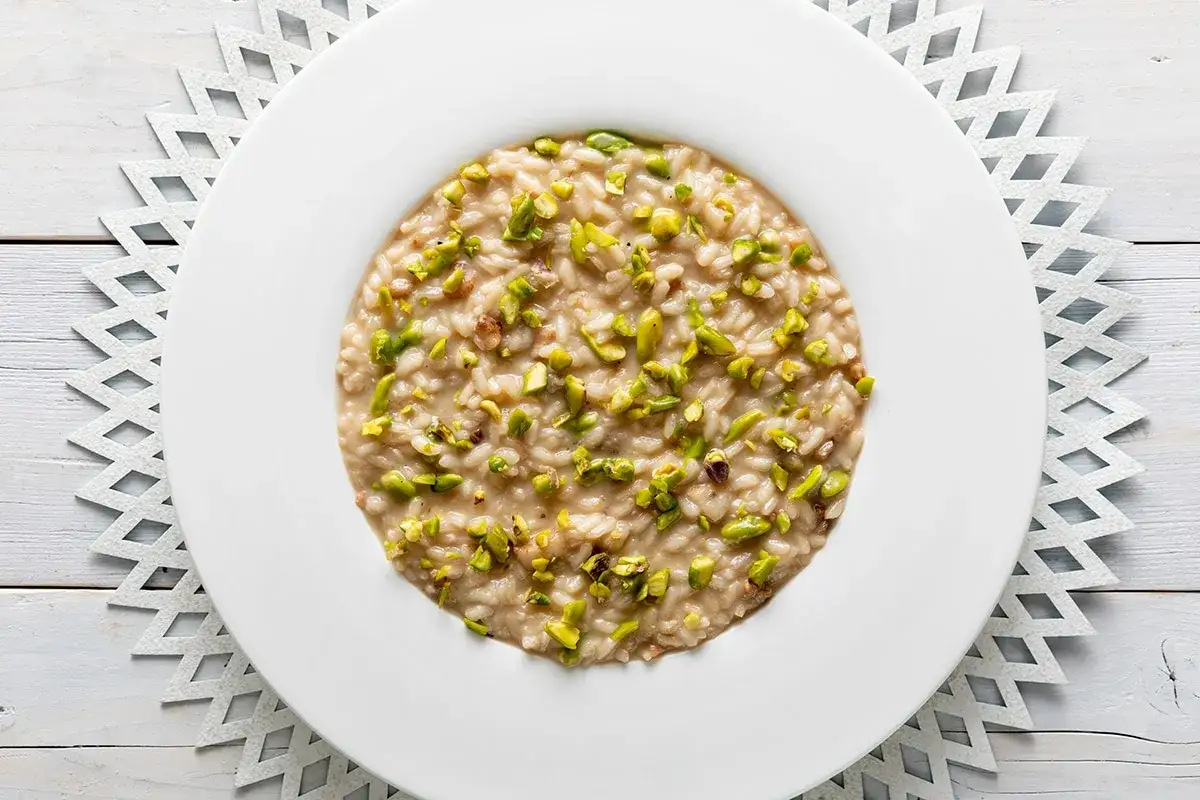 Un cremoso risotto al pistacchio, guarnito con granella verde brillante, servito su un piatto bianco.
