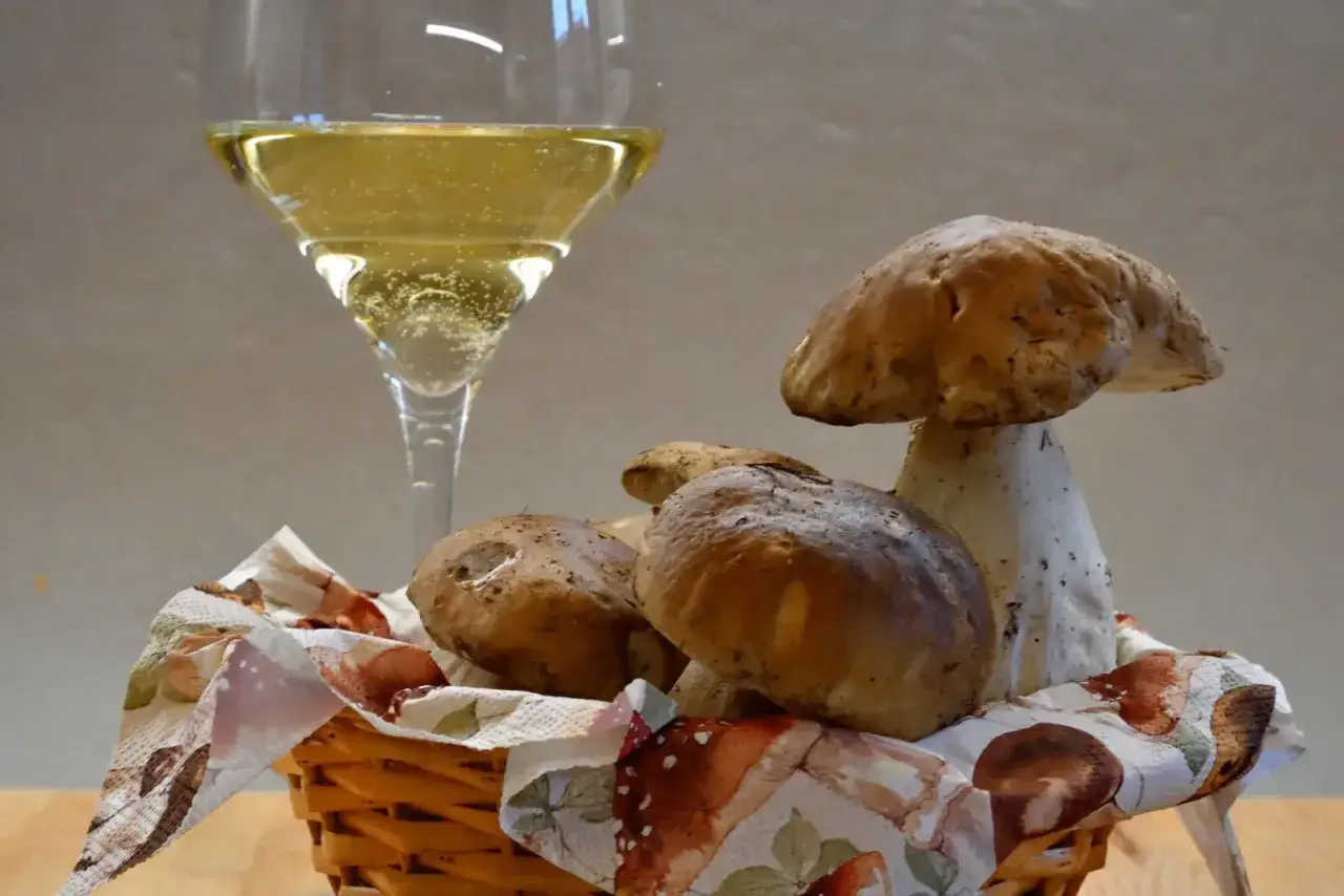 Un bicchiere di vino bianco frizzante, perfetto vino da abbinare ai funghi porcini appena raccolti, in un cesto decorato.