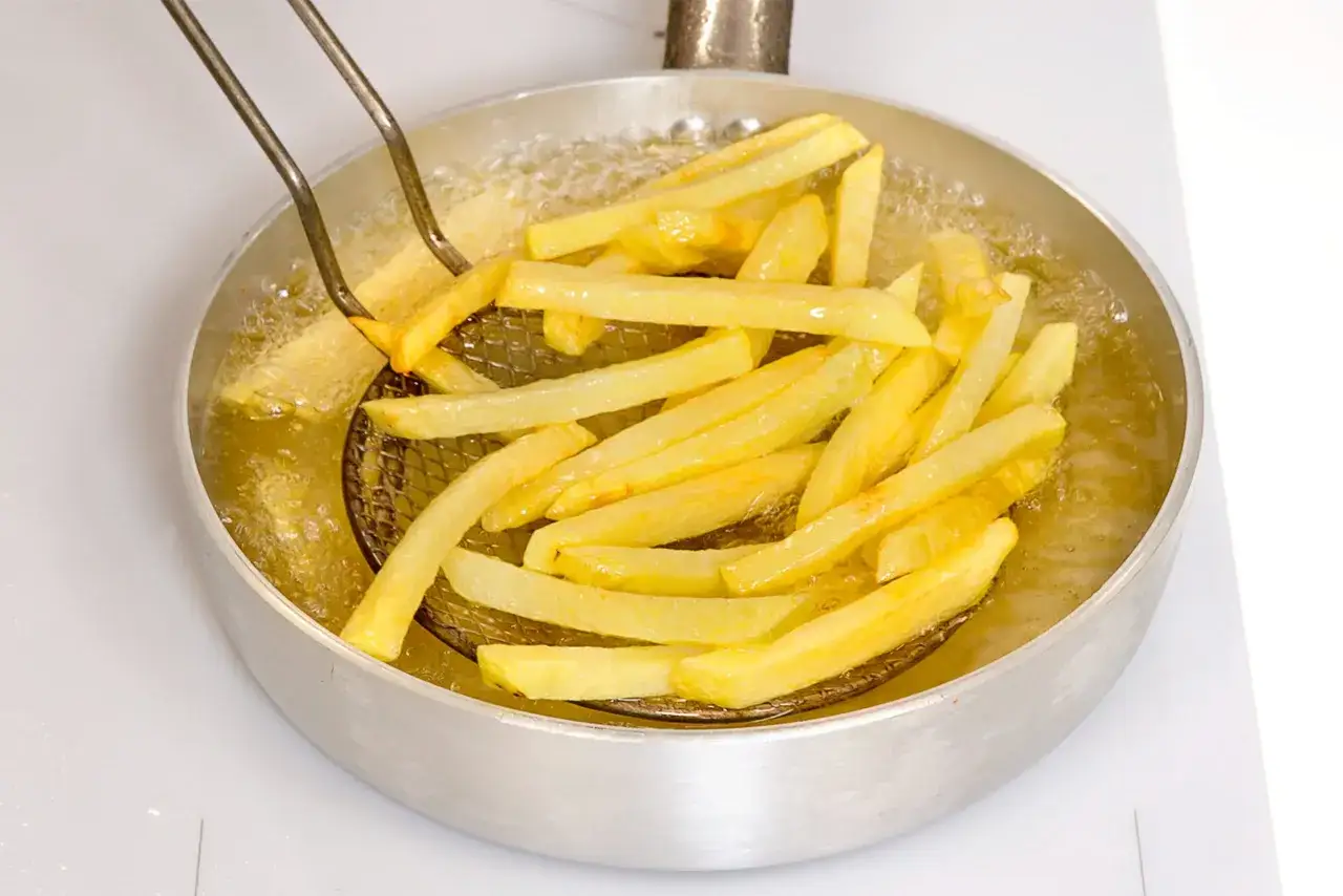 Patate fritte dorate che sfrigolano nell'olio bollente, pronte per essere gustate.
