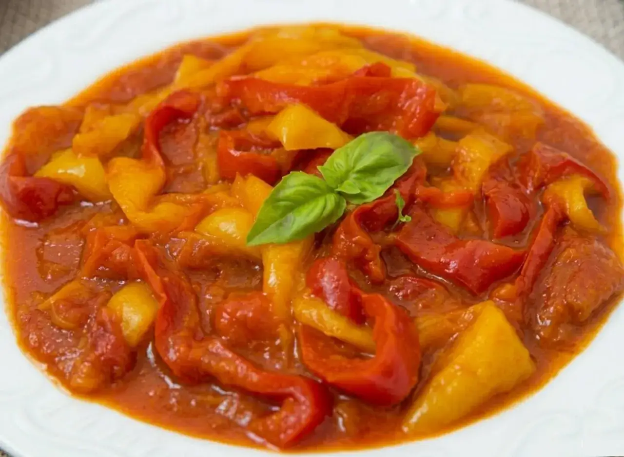 Peperonata ricetta della nonna: peperoni rossi e gialli cotti lentamente in un sugo saporito, guarniti con basilico fresco.