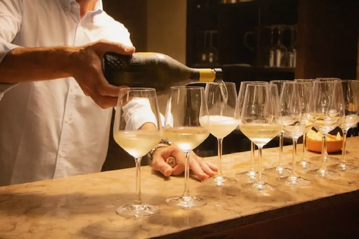 Un uomo versa vino bianco in una fila di calici, un'atmosfera da film sul vino.
