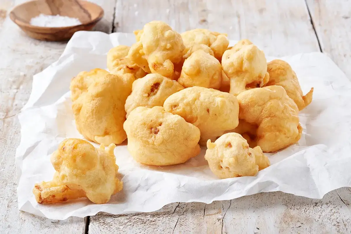 Un mucchio di delizioso cavolfiore fritto, dorato e croccante, servito su carta bianca.