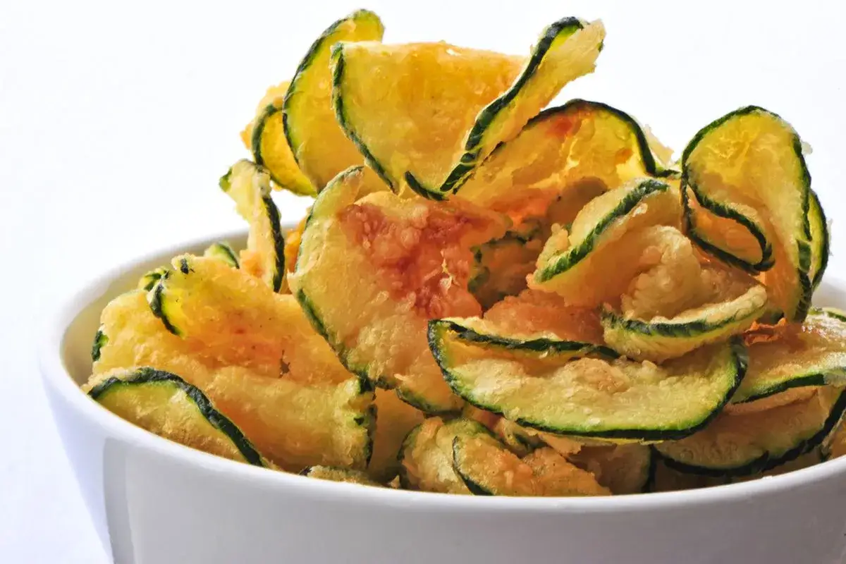 Fette croccanti di zucchine fritte in pastella, dorate e invitanti, servite in una ciotola bianca.