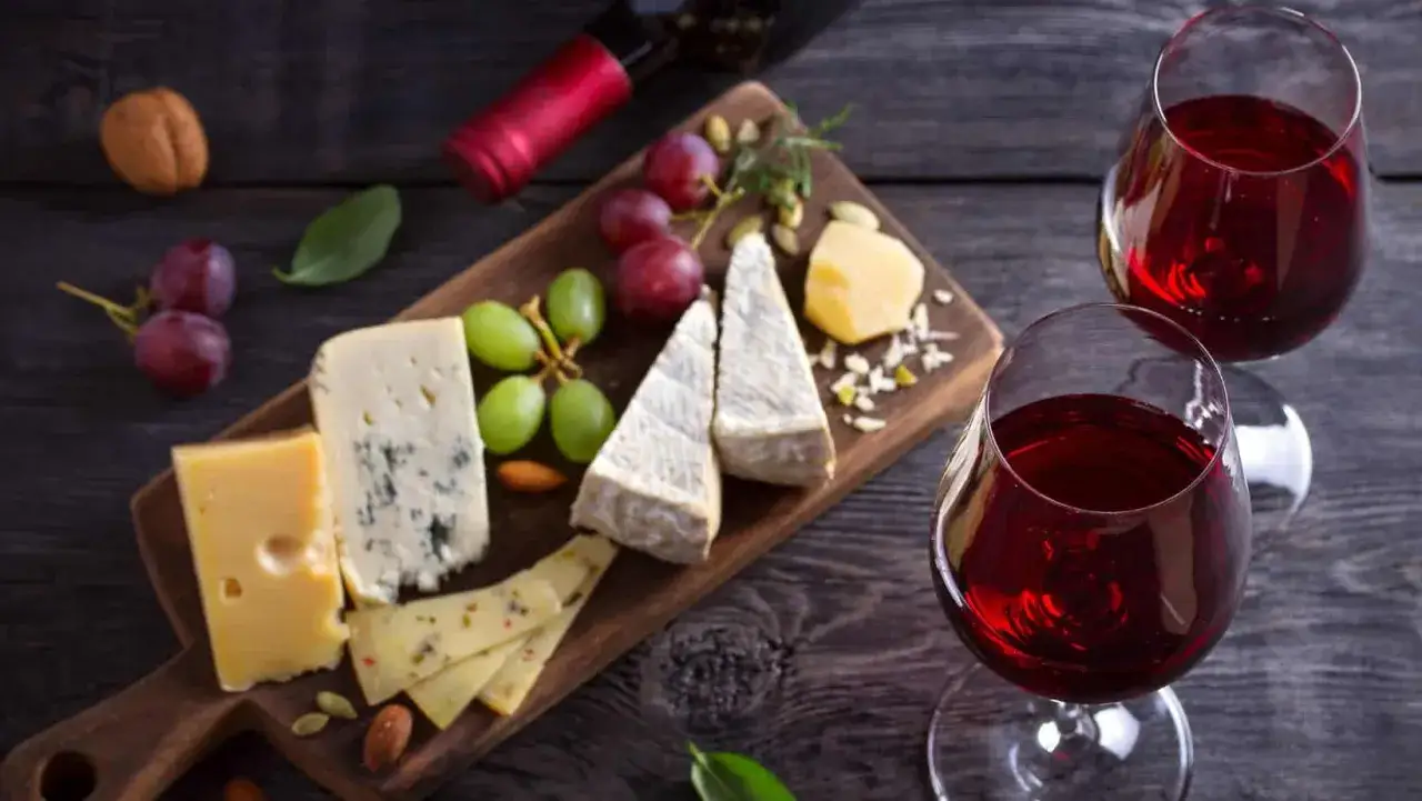 Tagliere di formaggi misti, uva e frutta secca, perfetti brunello di montalcino abbinamenti. Due calici di vino rosso completano la scena.