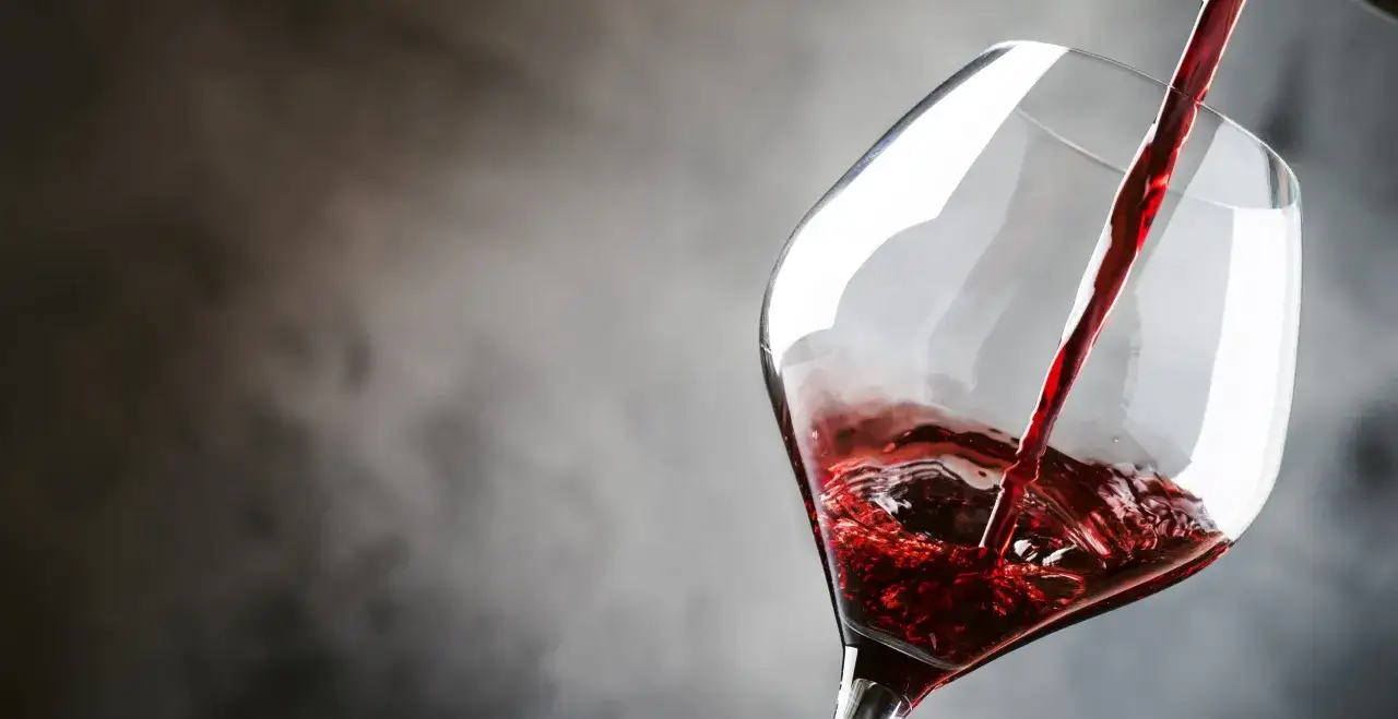 Versando vino rosso rubino in un calice, un'espressione del vitigno Barbera.