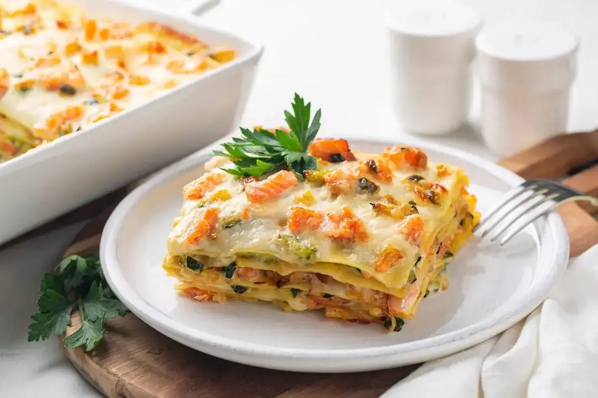 Porzione di lasagne di pesce con salmone e zucchine, guarnita con prezzemolo fresco.