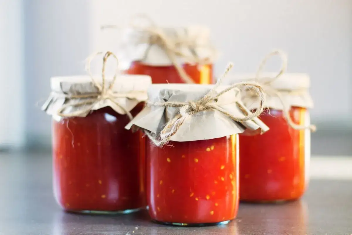 Quattro barattoli di conserva di pomodoro fatti in casa, chiusi con carta e spago.