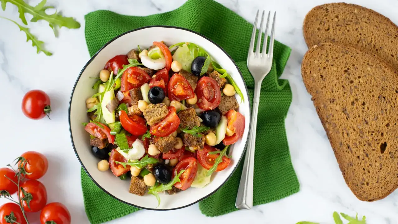 Una fresca panzanella napoletana con pomodori, cetrioli, olive, ceci e crostini, pronta per essere gustata.