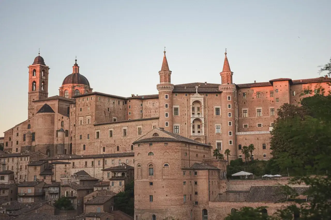 Palazzo Ducale di Urbino, una delle pi&ugrave; belle citt&agrave; da visitare in un giorno, con le sue torri e la cupola che si stagliano al tramonto.