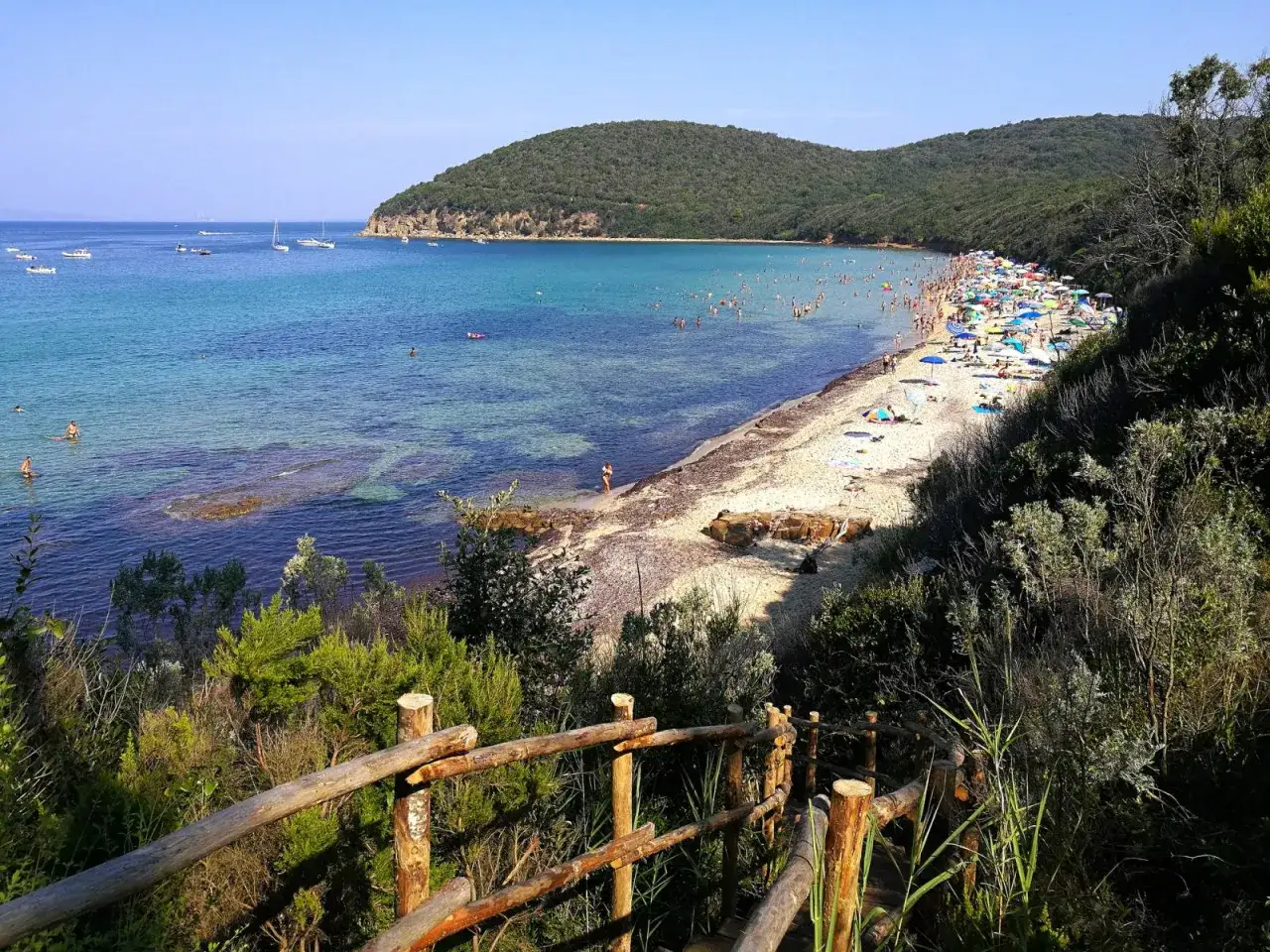 Vista panoramica della costa toscana, con una spiaggia affollata, mare cristallino e vegetazione rigogliosa. Una mappa ideale per sognare le vacanze.