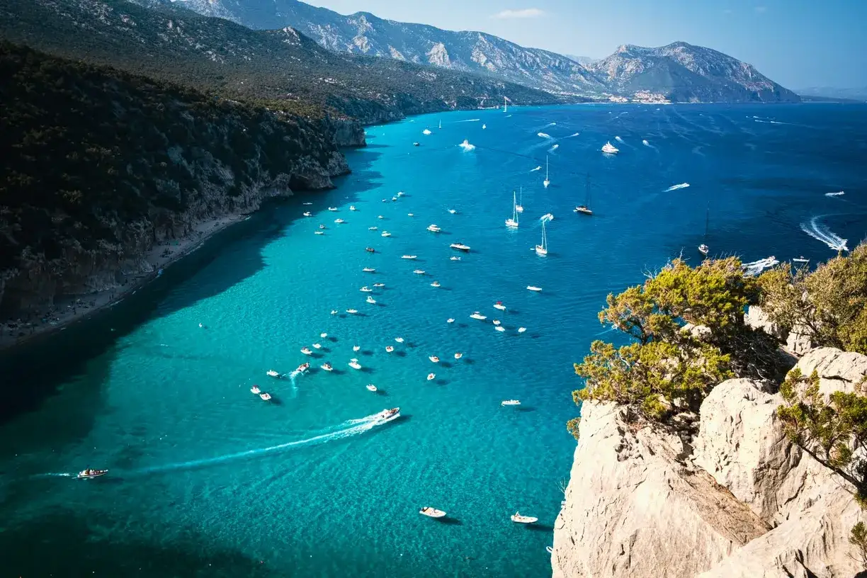 Baia con acque cristalline e montagne verdi, un vero paradiso. Molte barche navigano in quella che sembra la spiaggia pi&ugrave; bella Sardegna.