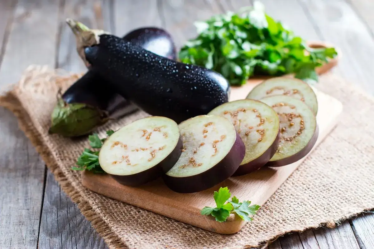 Melanzane fresche, alcune intere e altre affettate, pronte per essere cucinate. Un mazzetto di prezzemolo completa la scena, suggerendo la preparazione di un piatto gustoso.