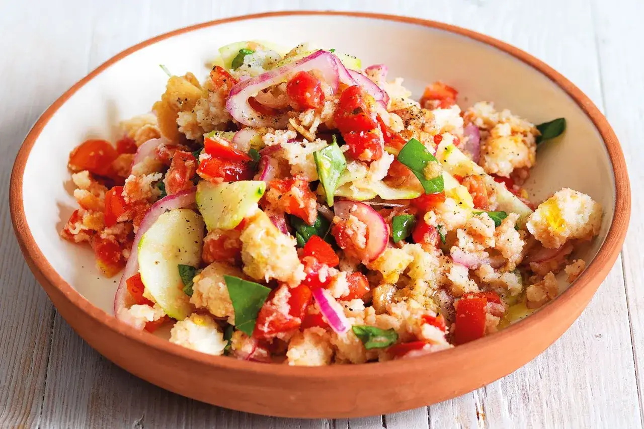 Panzanella salad with tomatoes, cucumber, red onion, and bread chunks in a terracotta bowl.