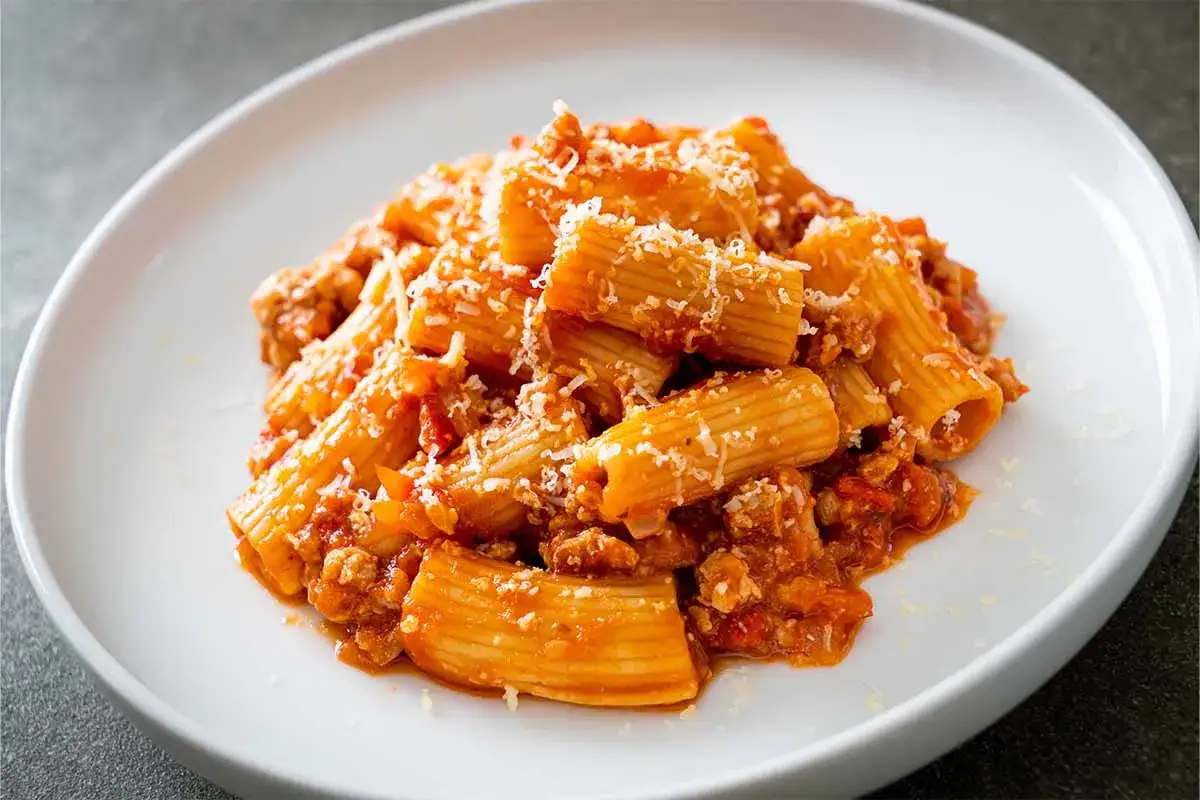 Rigatoni abbondanti conditi con un ricco sugo di carne e pomodoro, spolverati di parmigiano. Un piatto di pasta alla zozzona che fa venire l'acquolina in bocca.