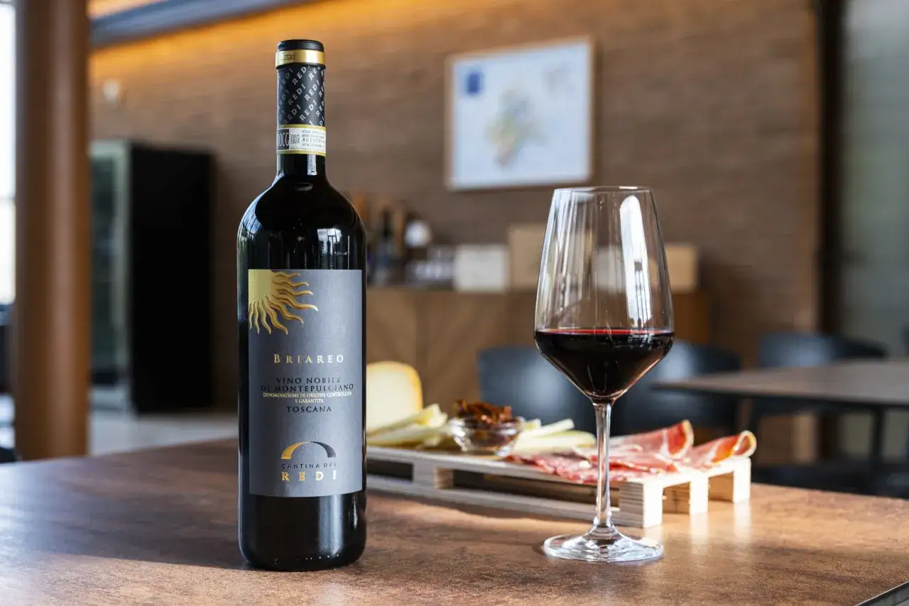 Un calice di Vino Nobile di Montepulciano e una bottiglia, perfetti per una visita cantine Montepulciano. Tagliere con salumi e formaggi.