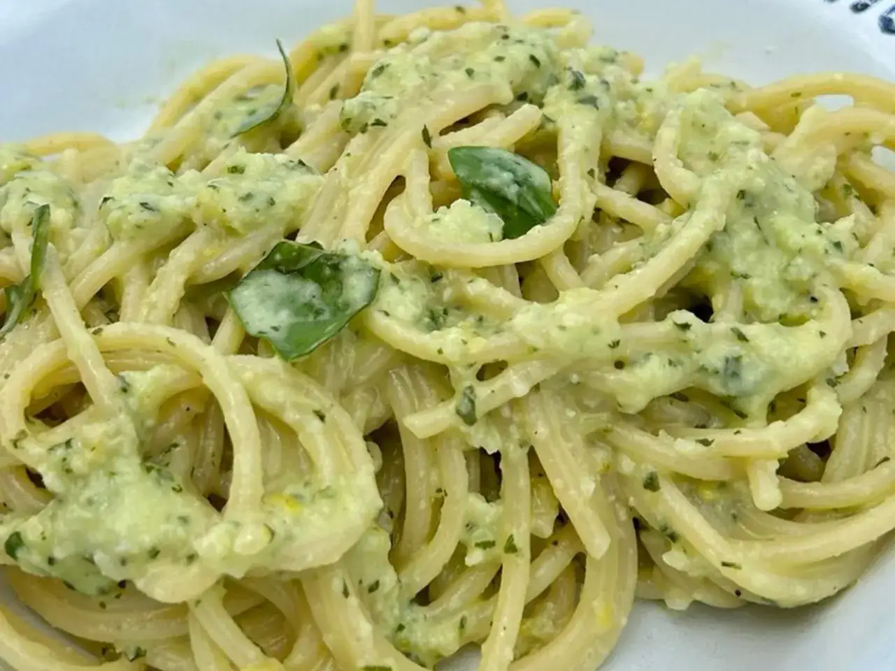 Spaghetti conditi con un cremoso pesto al limone, profumato e fresco, con foglie di basilico.