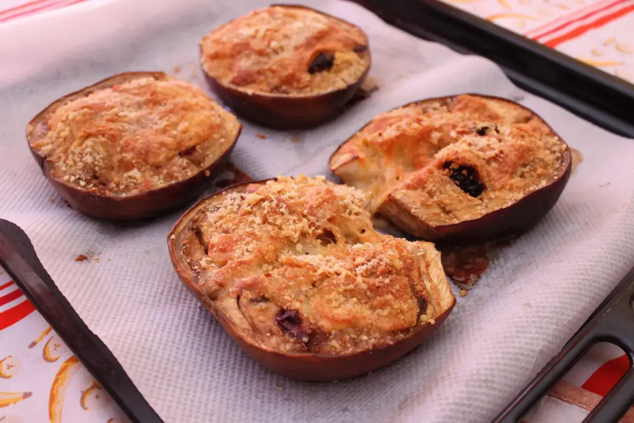 Quattro deliziose melanzane ripiene pugliesi, appena sfornate, su una teglia.
