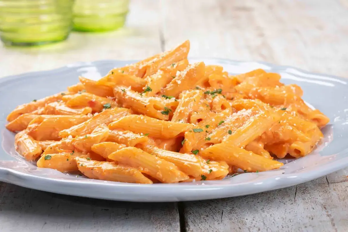 Penne cremose con salsa rosa, un classico tra le ricette con la pasta, guarnite con prezzemolo e parmigiano.