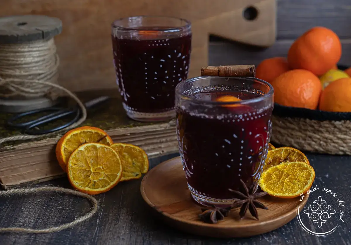 Caldo vin brul&eacute; in bicchieri decorati, con arance, spezie e un libro antico. Un invito al tepore invernale.